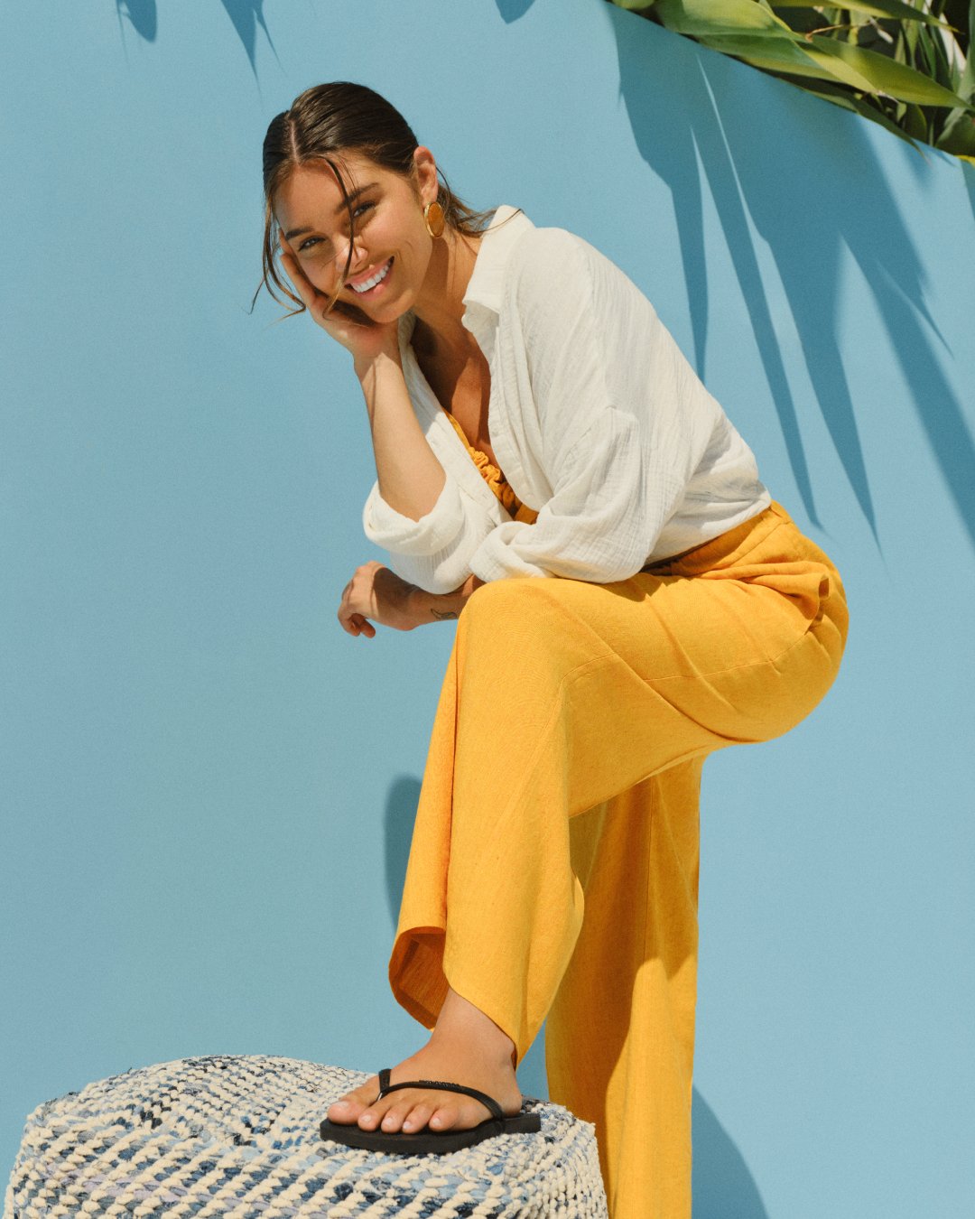 woman in white shirt and yellow pants, leaning over a chair, wearing black havaianas slim flip flops