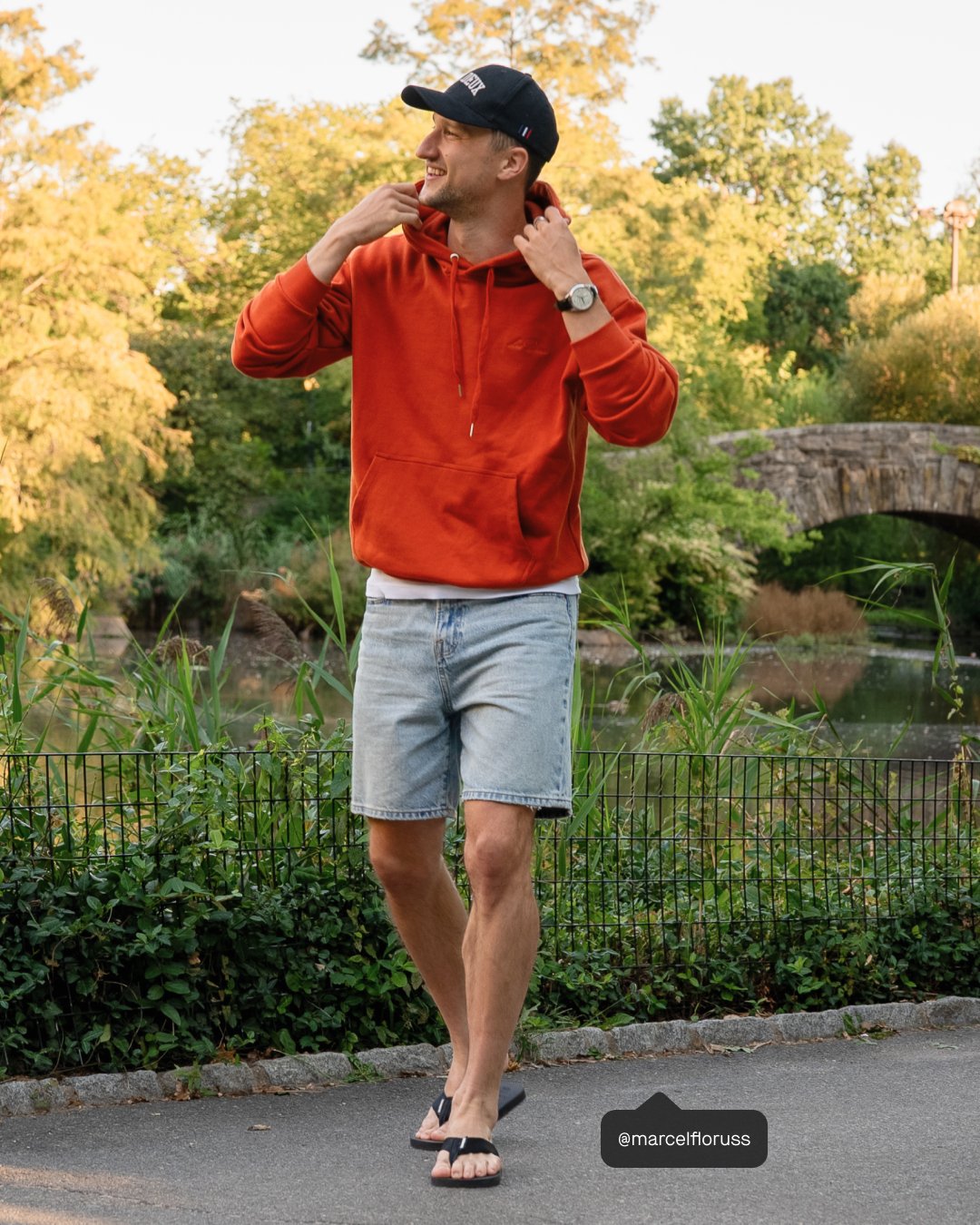 man walking in a park wearing a red hoodie, jean shorts, and black havaianas flip flops