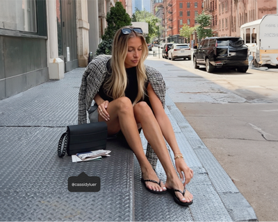 girl sitting on a street step wearing black flip flops and a black clutch