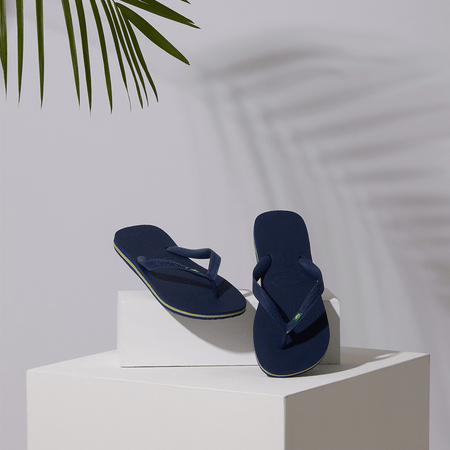 Navy blue women's flip flop with Brazil flag on strap posed on white block with palm leaves