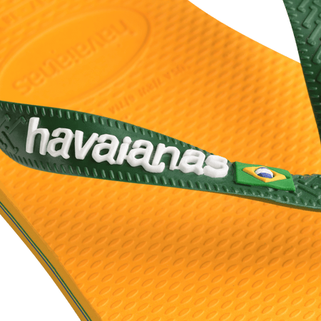 yellow flip flops with green straps featuring a brazil flag, zoomed in on the green strap with havaianas written in white and the brazil flag