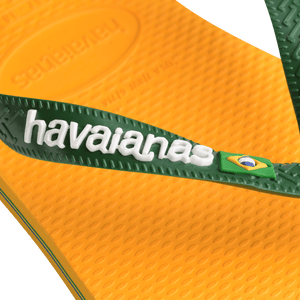 yellow flip flops with green straps featuring a brazil flag, zoomed in on the green strap with havaianas written in white and the brazil flag