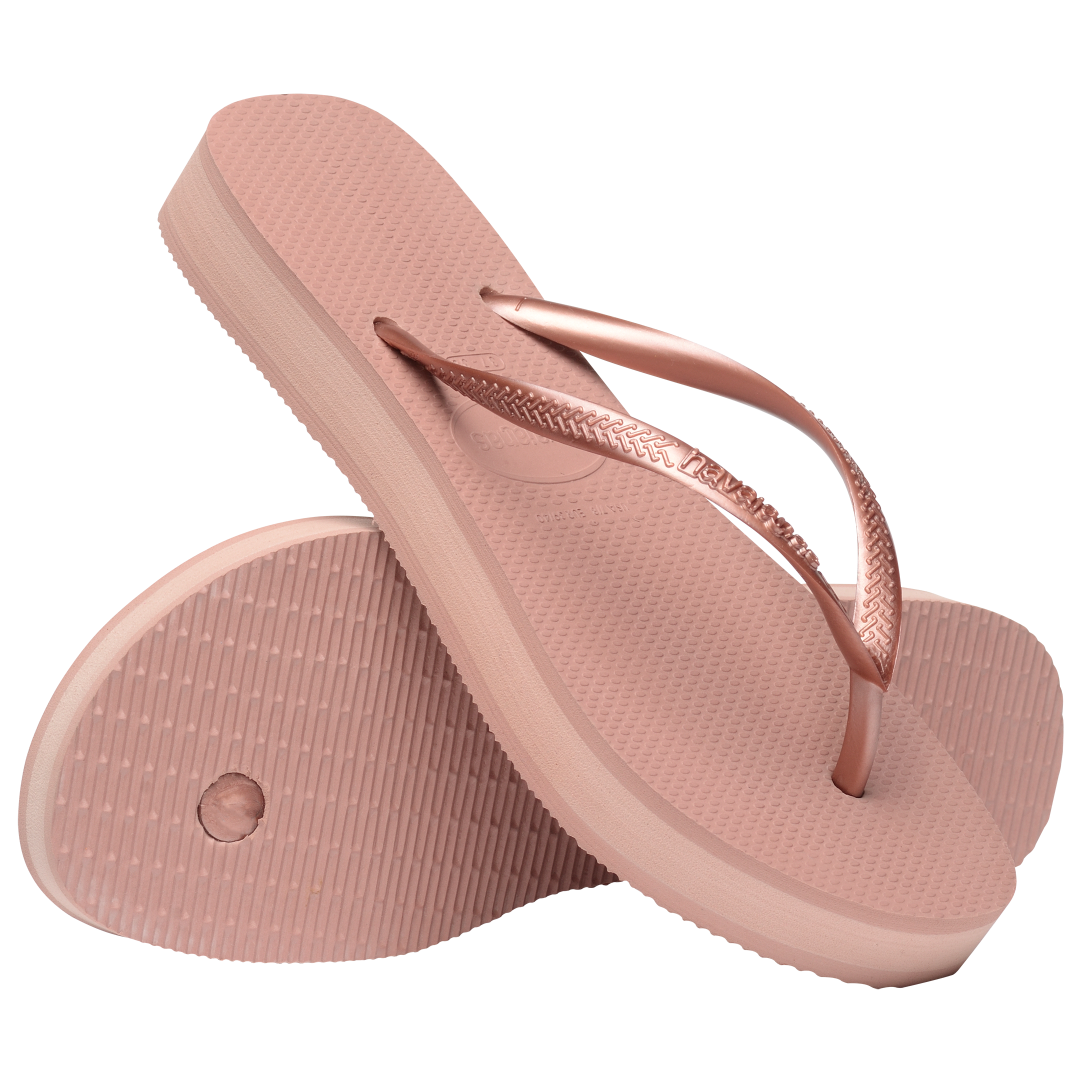 light pink flip flops with a platform and a pink metallic strap, one sandal balancing on the other, toe side down