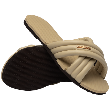 Cream criss-cross strap slide sandal with right shoe perched on left view showing brown sole