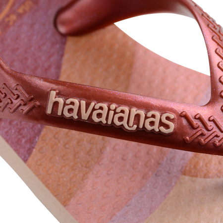 Baby flip flops in pink, beige, orange print, zoomed in on havaianas logo on pink metallic strap 