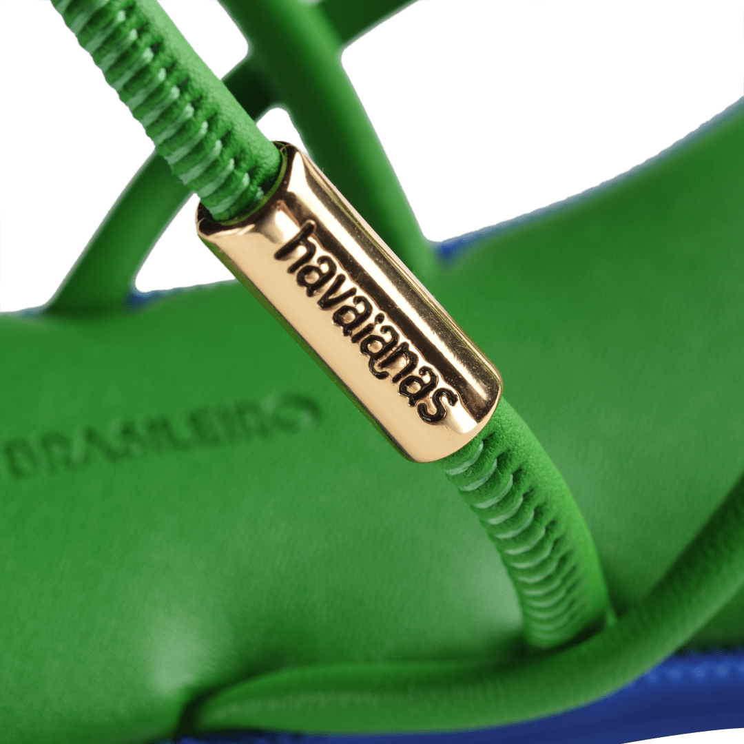 Green strappy sandal with blue sole and gold logo detail on strap