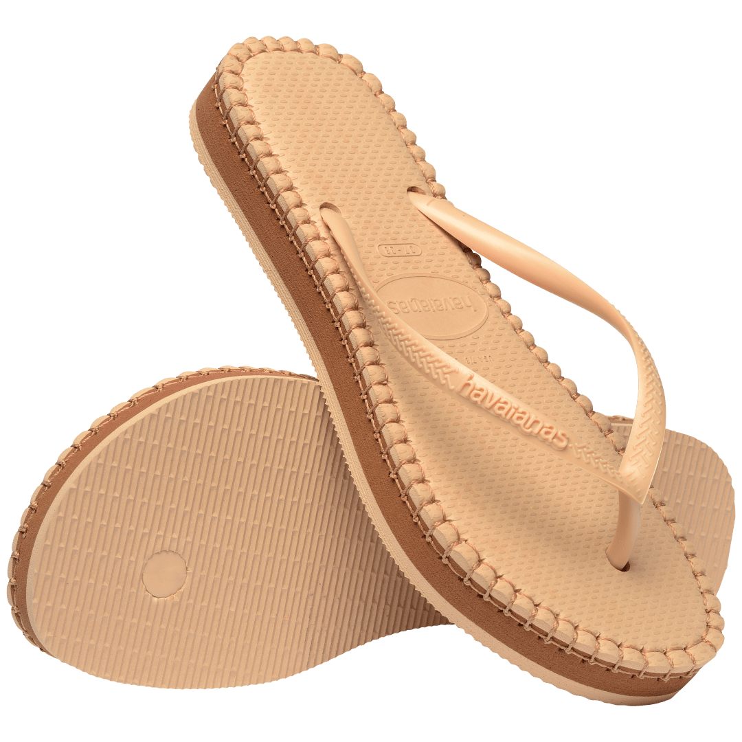 beige sandal with darker brown stitching and a dark brown midlayer between the sole and bottom of shoe, one sandal leaning on the other, toe side down