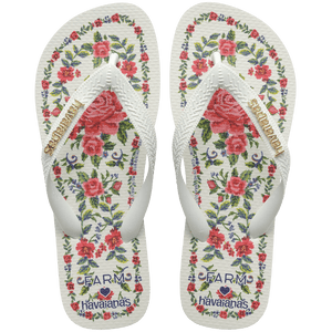 flip flops with pink flowers on a white background with white straps with a gold havaianas logo on them, top facing