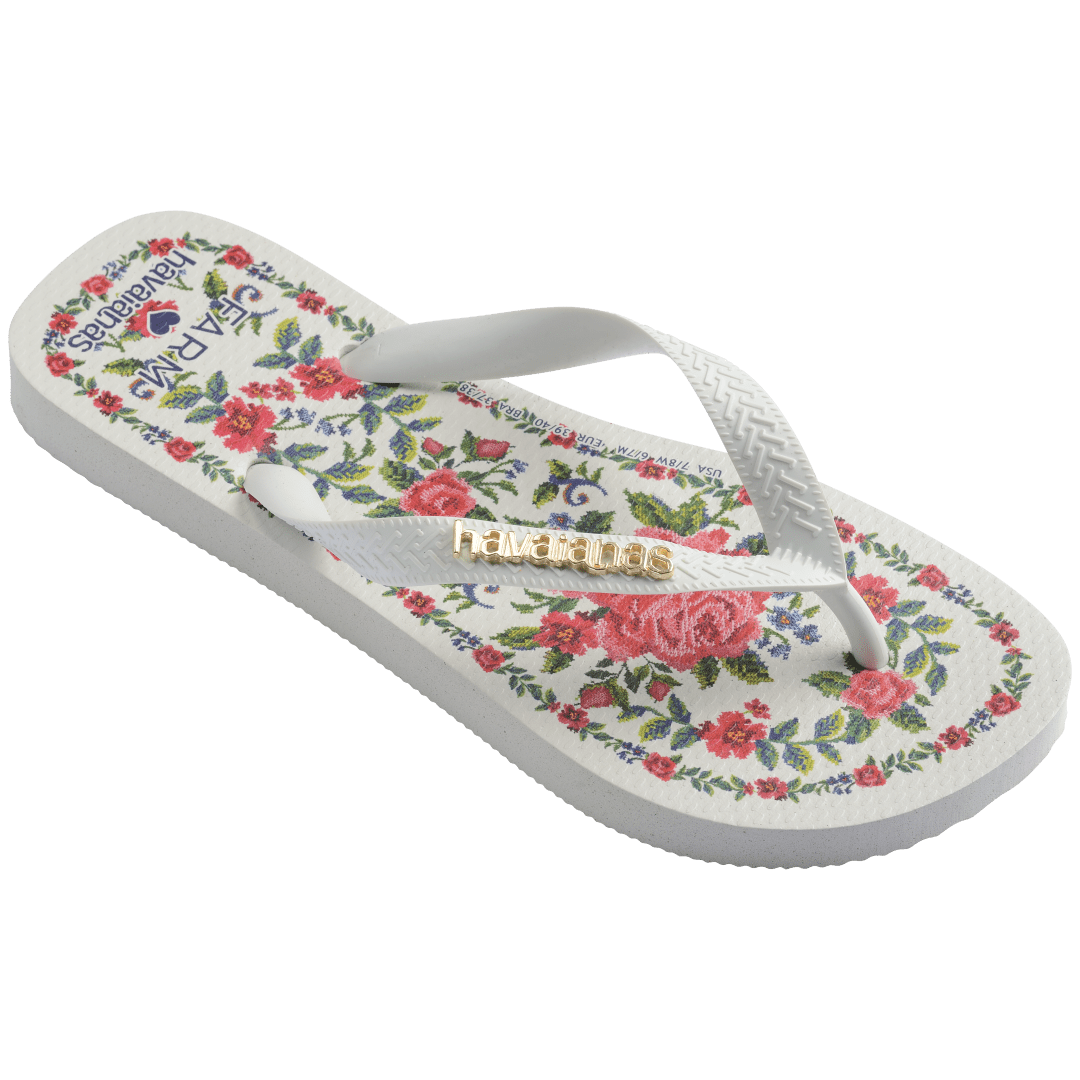 flip flops with pink flowers on a white background with white straps with a gold havaianas logo on them, front-right facing