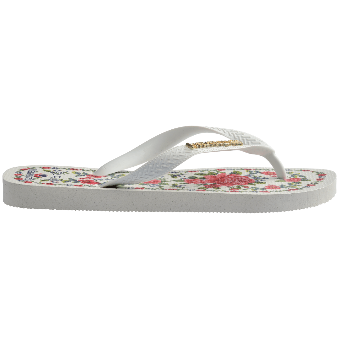 flip flops with pink flowers on a white background with white straps with a gold havaianas logo on them, side facing