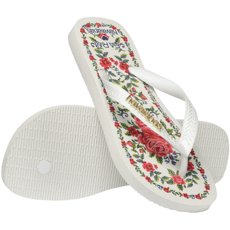 flip flops with pink flowers on a white background with white straps with a gold havaianas logo on them, one flip flop resting on the other, toe side facing down