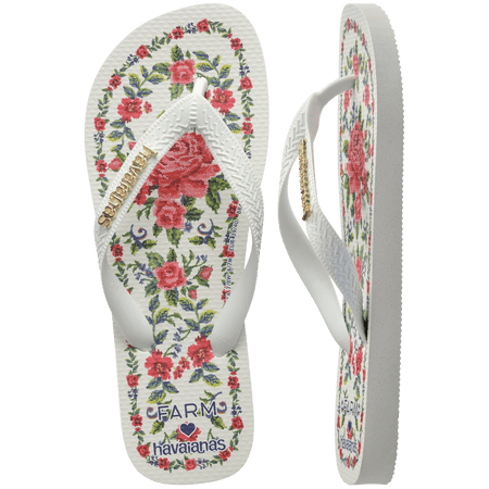 flip flops with pink flowers on a white background with white straps with a gold havaianas logo on them, one top facing and one side facing