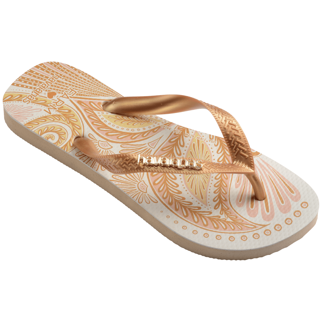 flip flops with gold and light pink abstract print and metallic gold straps with a metal havaianas logo, front, diagonal side facing