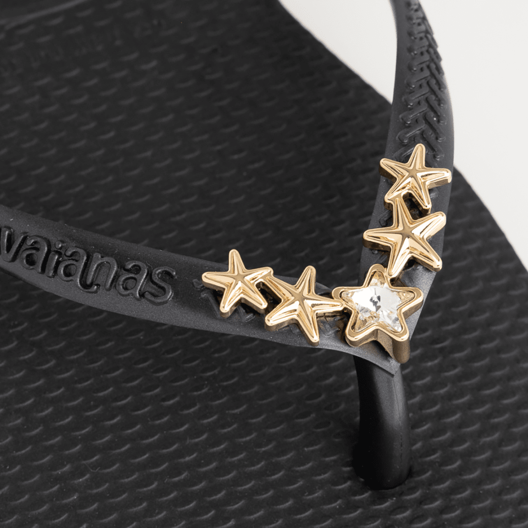 Women's black flip flops with gold star charm embellishment, detail view