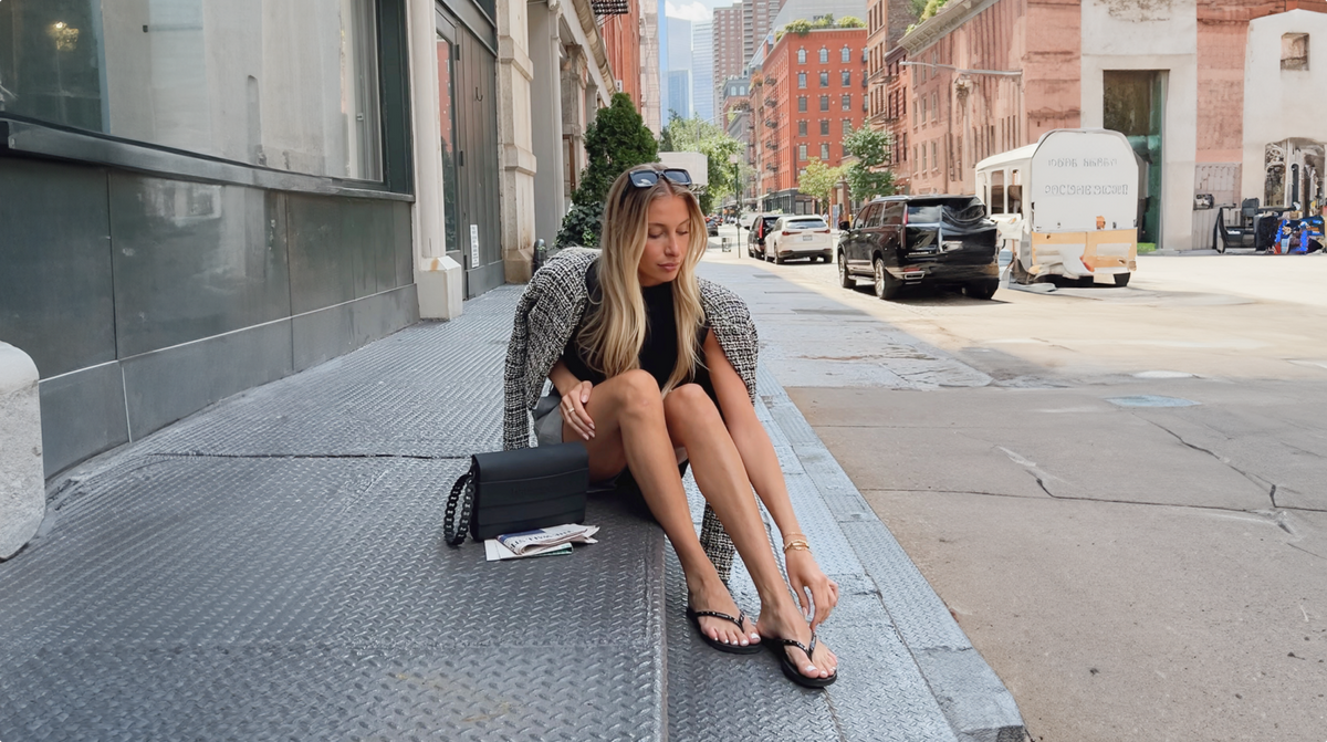 girl sitting on a street step wearing black flip flops and a black clutch