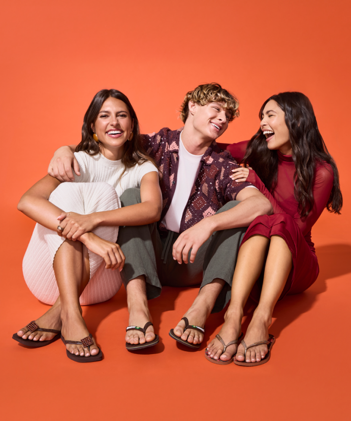 girl in orange tank top and jean shorts, sitting on a ledge, wearing black havaianas slim flip flops