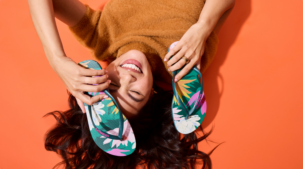 girl holding green flip flops with flowers printed on them over her face